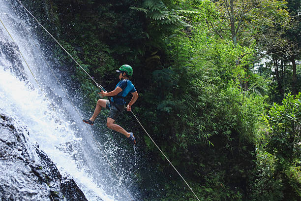 Dynamic Shot Of Male Adventurer In Green Helmet Bounding Off Waterfall Rock Face During Rappel