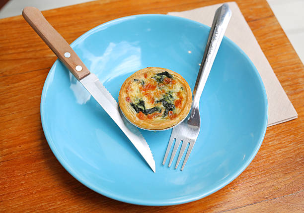 A freshly baked mini spinach and cheese quiche served on a bright blue plate with cutlery.