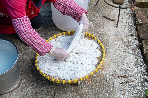This image captures a worker arranging fresh noodles on a bamboo tray, highlighting the meticulous care taken in the noodle preparation and drying process.
