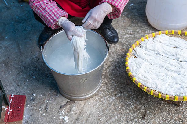 A skilled worker soaks fresh noodles in a bucket of water, demonstrating the traditional noodle-making process and the importance of hydration for these culinary treats.