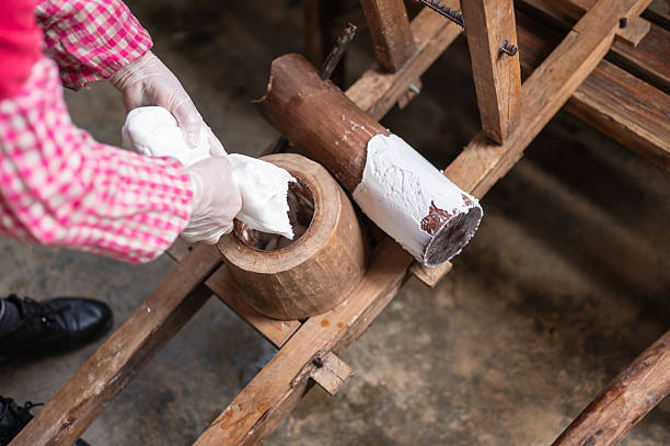 An adult worker operates a manual lever press to produce fresh noodles in a traditional food workshop. The image emphasizes craftsmanship, skill, and the heritage of handmade noodle production.