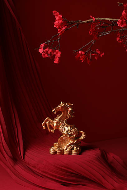 Golden horse figurine standing on coins against red fabric and cherry blossom branch.