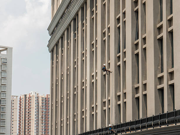 Window washer cleaning modern office building windows. High-rise window cleaners using rope access. Industrial alpinist washing skyscraper exterior. Dangerous work at height.