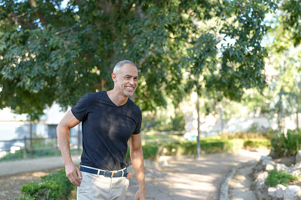A man in a black shirt and tan pants is smiling and walking down a path. Scene is cheerful and relaxed