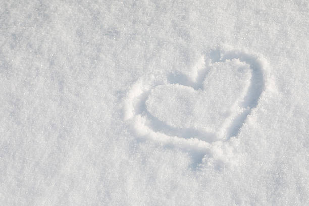 A snow heart is drawn in the snow. The heart is surrounded by snow and he is a symbol of love