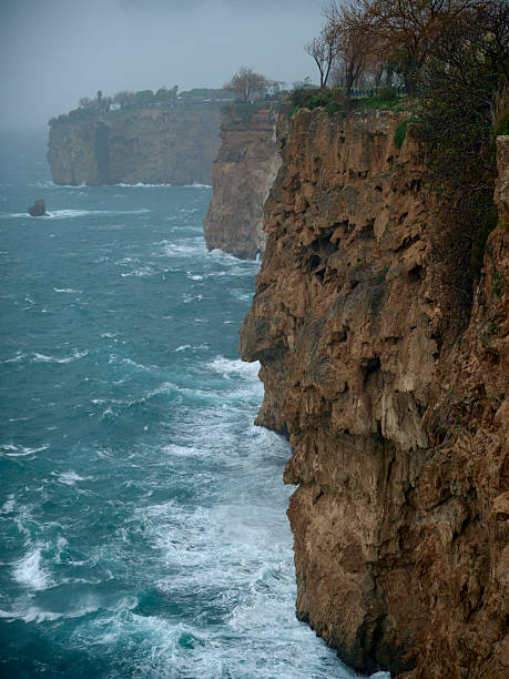 High angle view of steep coastal cliffs with white crashing waves on a rainy day.