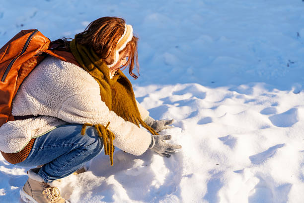 Young beautiful woman with long blond hair at walk on a frosty day in a winter park. She is posing and having fun with еру big snowman. Shooting outdoors on a sunny day