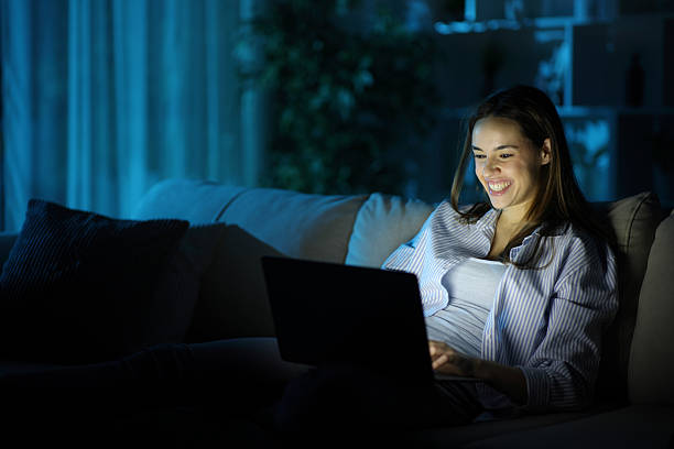 Happy woman in the night using personal computer sitting on a couch at home