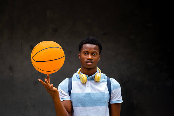 Young man wearing headphones and backpack spinning basketball on finger while looking at camera