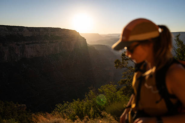 Female hiker with backpack standing on a viewpoint overlooking the Grand Canyon. Travel, adventure, hiking, and outdoor exploration concept in a natural desert landscape under a clear blue sky.