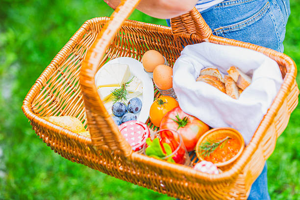 Wicker basket filled with fresh fruits, vegetables, and bread on a grassy field.