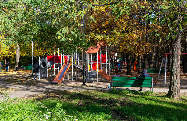 Little child wearing a blue hat and winter coat walking on wood chips in outdoor playground on a sunny day. Scanned from analog film