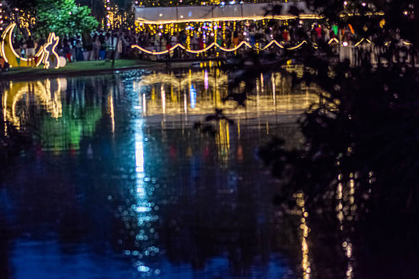 People gather at a public park during a nighttime festival featuring decorative lights reflected on the water. The scene captures urban leisure and social activity in an outdoor event setting. in Bangkok, Thailand, on December 6, 2025.