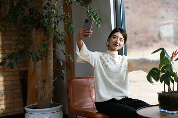 Young woman is using smartphone to take selfie by the window