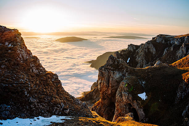 Warm sunlight illuminating steep mountain cliffs and grassy slopes above a thick cloud inversion stretching across the horizon.