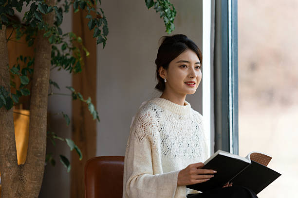 Young woman is reading book by the window