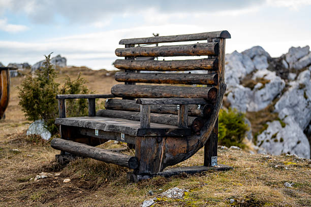 Handcrafted wooden bench placed in an open mountain landscape, surrounded by rocks, grass, and a calm natural atmosphere.