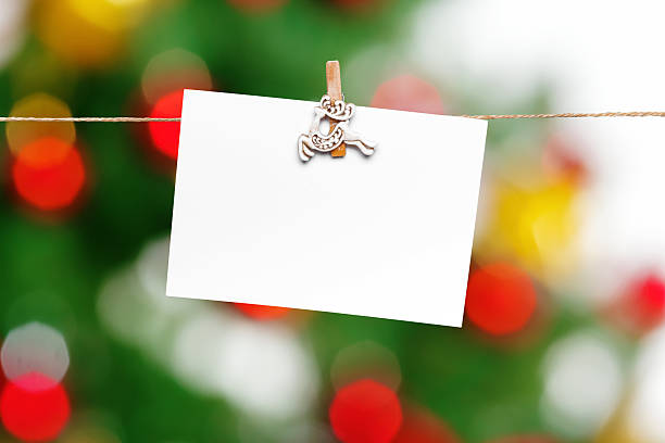 A blank card is clipped to a string with festive lights and decor in the background.