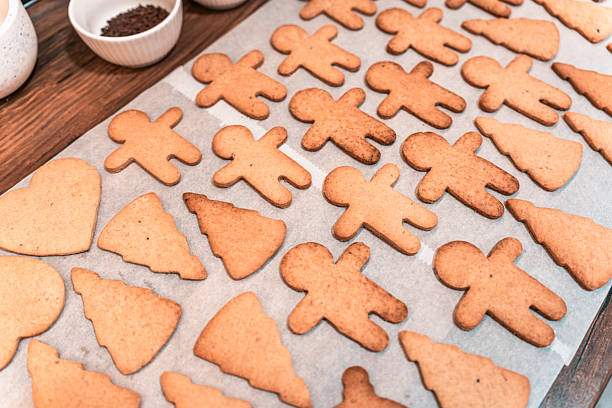 Gingerbread cookies in various shapes including gingerbread men and Christmas trees are arranged on parchment paper ready for baking. These homemade treats are the holiday season and festive celebrations.