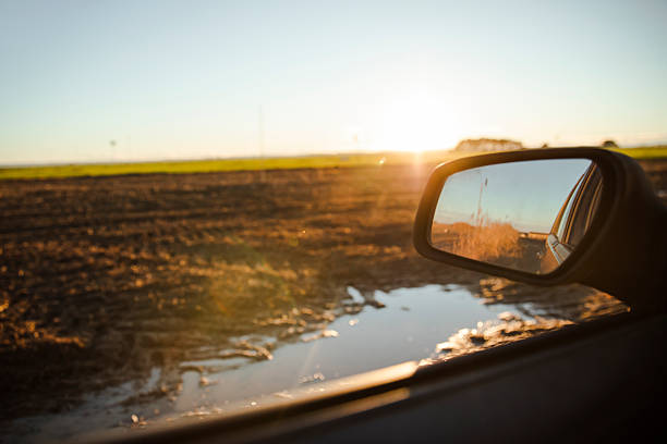 View of a muddy rural road with puddles at sunset, seen from inside a car. Travel concept, countryside journey and peaceful evening atmosphere