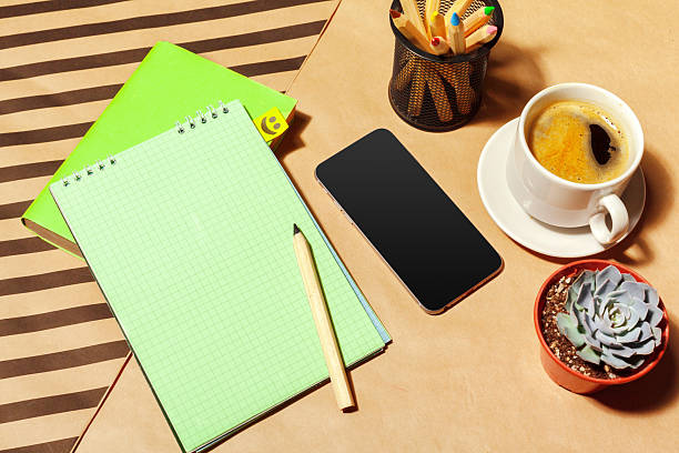 Person enjoys coffee while working with a notebook and smartphone on a wooden table.
