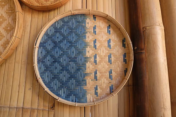 Handmade woven rattan baskets in various sizes arranged on a bamboo surface with a blue woven basket in the center and green leaves on the left side, showcasing rustic natural interior decoration.