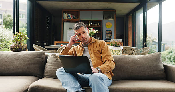 istock Remote work, laptop and man on sofa thinking for online article, research and proofreading. Freelancer, living room and mature person on computer for editing report, story ideas and planning in home 2255893571