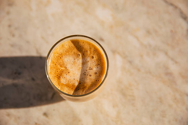 flat lay of a banana smoothie with peanut butter and cocoa, served with a straw, isolated on a gray background with copy space.