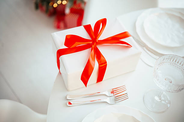White gift box with red ribbon on table with plates and forks, festive occasion, elegant table setting