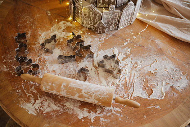 Cookie cutters scattered on flour dusted wooden table with rolling pin and festive lights