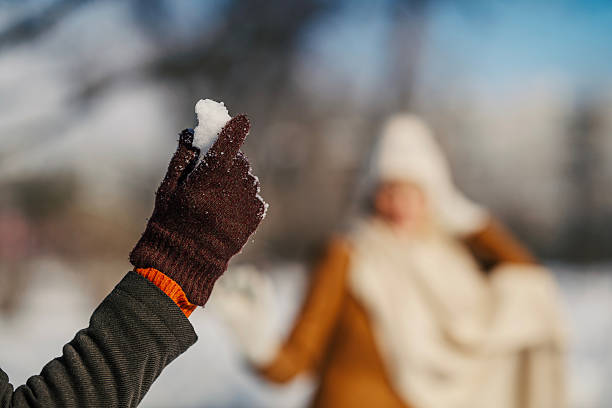 Unrecognizable hand in glove reaching for falling snowflakes, blurred forest backdrop eco-tourism