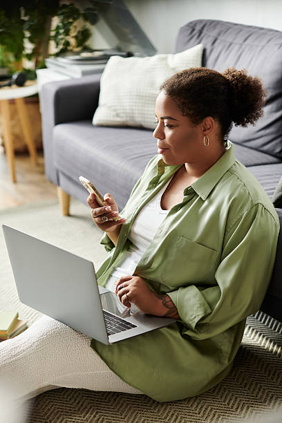 Curly-haired woman multitasking with her phone and laptop in a modern apartment
