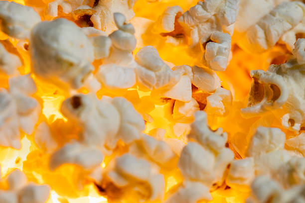 Warm, fluffy popcorn is piled high in a container at a bustling movie theater. The scent fills the air as guests prepare for an exciting film experience in the evening.