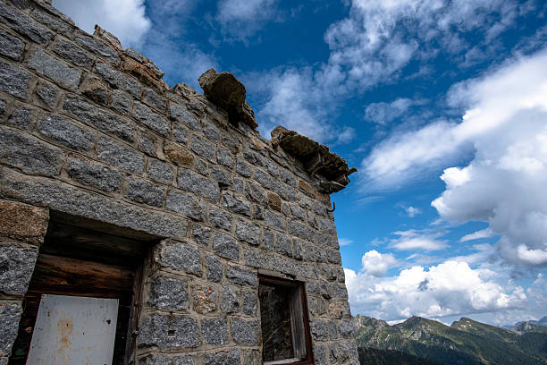 Abandoned stone ruin in the Lagorai mountains, Trentino, Italy, surrounded by wildflowers and rocky peaks under dramatic storm clouds.