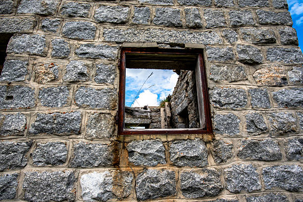 Old stone wall of an abandoned alpine hut in the Lagorai mountains, Trentino, Italy, with a window opening framing the sky and ruins.