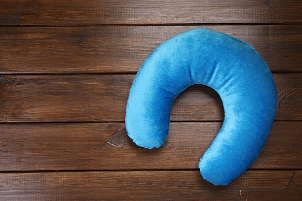 Light blue travel pillow on wooden table, top view. Space for text