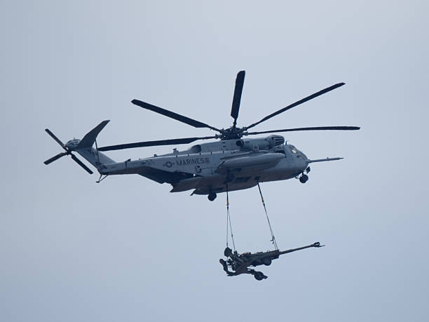 San Diego, California, USA - September 28, 2025: A detailed view of a US Marine Corps CH-53E Super Stallion heavy-lift helicopter transporting an M777 howitzer artillery piece using an external sling load.