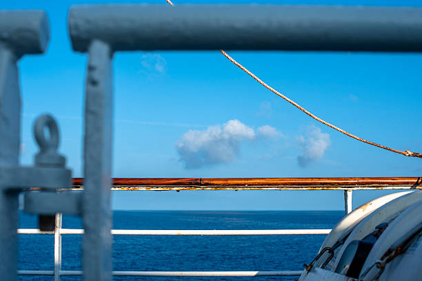 Metal railings and a rope line on a ferry near Corsica, with the sea and clouds in the background. Clean nautical composition with subtle rust details.