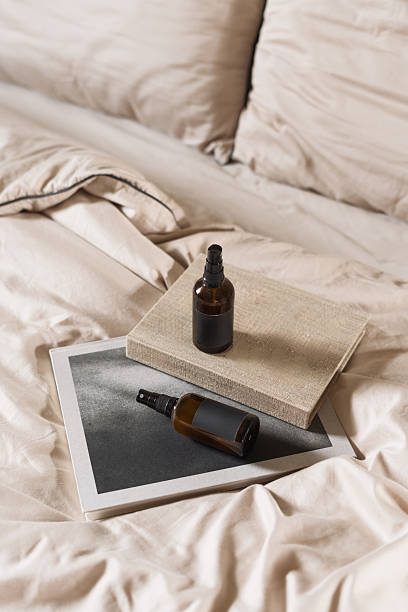 A serene bedroom features soft beige bedding and decorative pillows. An arranged stack of books and spray bottles with lavender and herbs add a touch of style and invite relaxation in hotel room