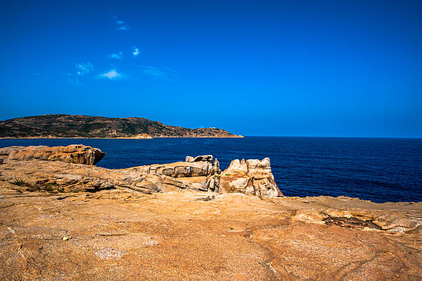 Wide rocky plateau above the Mediterranean sea with distant hills under clear blue sky in Corsica, France. Natural textures, strong foreground and serene coastal atmosphere.