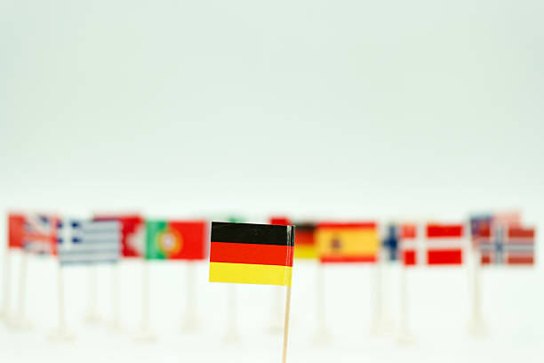 Small flags from various countries are arranged on a table with the German flag prominently displayed. Some flags are in the background, showing diversity.
