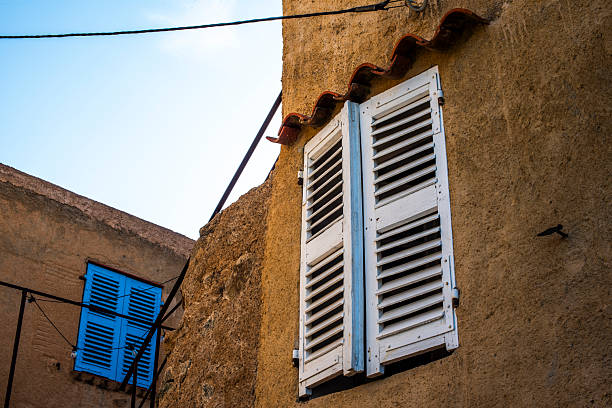 Traditional Mediterranean house facade with weathered shutters in Corsica, France. Rustic textures, pastel colors and soft daylight evoke Southern European architecture and slow village life.