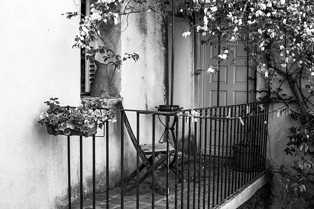 Warm Mediterranean balcony with plants, iron railing and small table in Corsica, France. Soft natural light, earthy tones and rustic textures evoke slow living and Southern European charm.