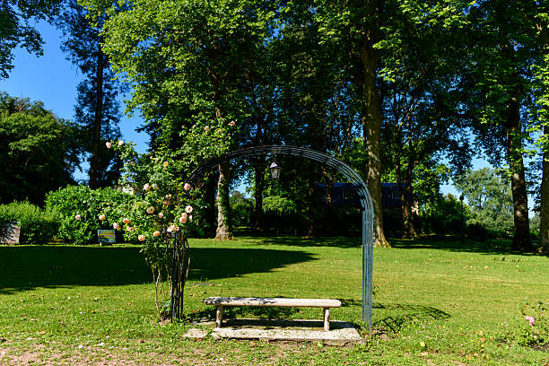 Photo showing a large, lengthy metal pergola archway that has been planted with trained espalier apple and pear trees, as well as some fruiting grape vines.  This ornamental garden tunnel is underplanted with herbs and summer bedding flowers, with an old block paved red brick pathway leading to a distant lawn and orchard at the other end of the garden.