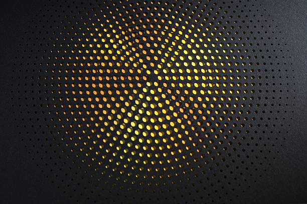 Still life photograph of an abstract cut paper artwork featuring a radial perforated pattern. Warm golden light shines through circular cutouts on dark paper, creating a modern, minimal, and elegant fine art background with strong texture and contrast.