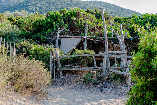 Rustic wooden fence and natural shelter along a sandy path in Corsica, France. Mediterranean vegetation, wild landscape and tranquil outdoor atmosphere in a remote coastal area.