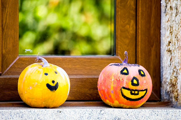 Painted Jack-o-Lantern Pumpkin figurines close-up view on window sill, leaves reflections. Galicia, Spain. Monster shape, scary.