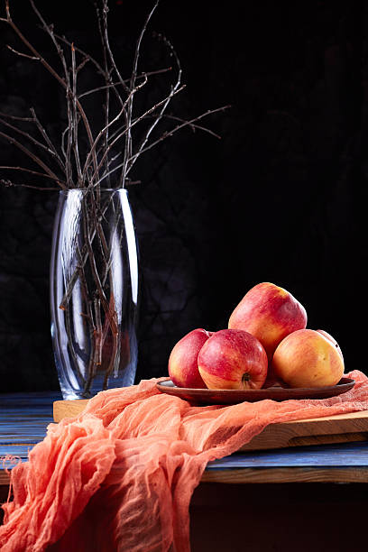 Red apples on a clay plate on gauze and vase on a dark background
