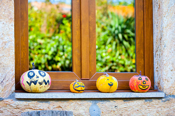 Painted Jack-o-Lantern Pumpkin figurines close-up view on window sill, leaves reflections. Galicia, Spain. Halloween decoration.