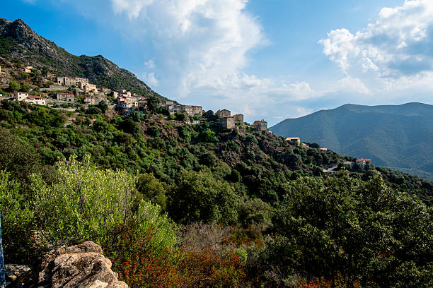 Mountain village perched on a green hillside overlooking a wide valley. Scenic Corsican landscape in France, conveying scale, remoteness and the relationship between human presence and wild nature.